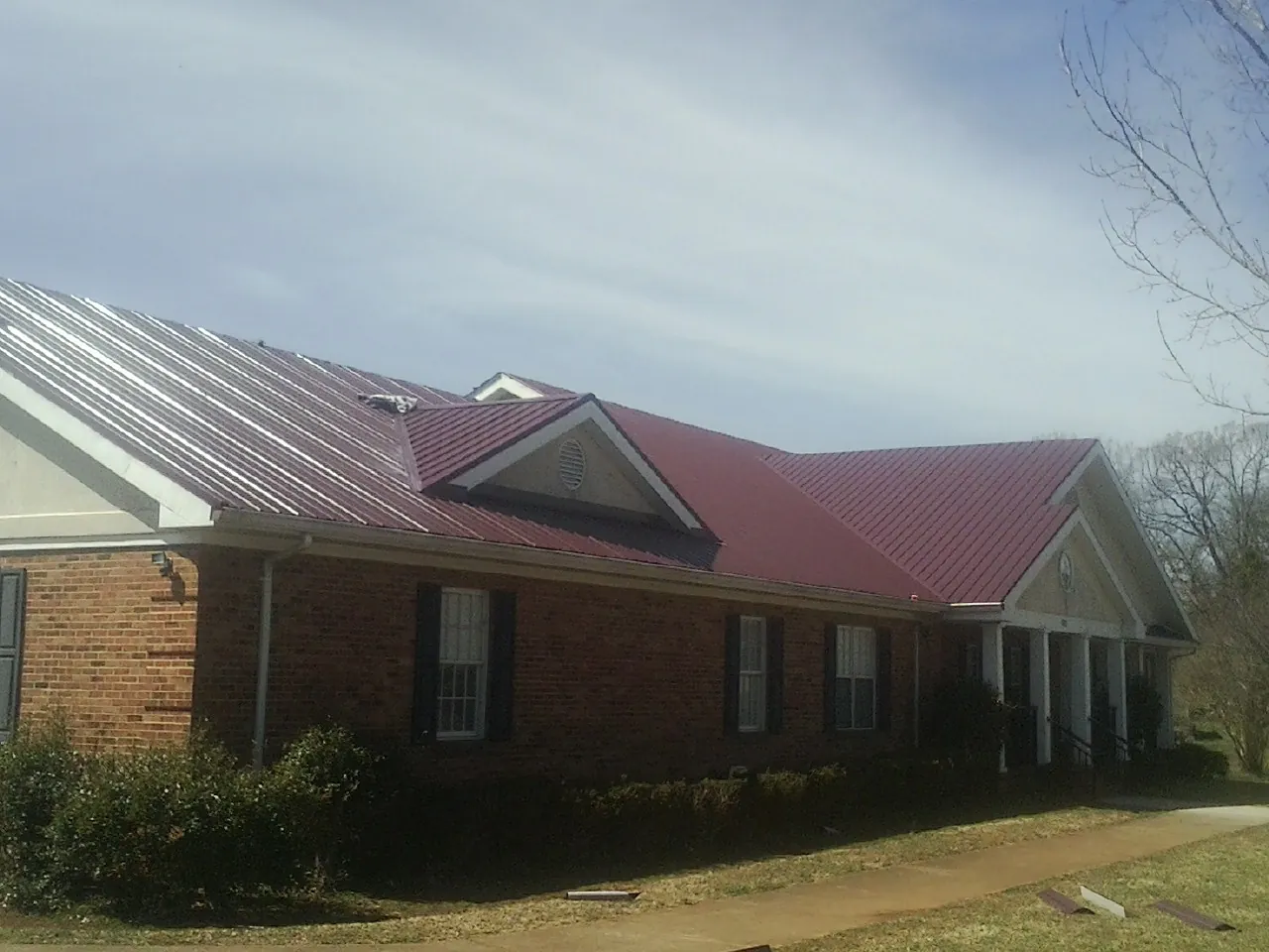 Red metal roof with gabled entries on a long brick building, from a Hail Damage Roof Repair job in Dunedin