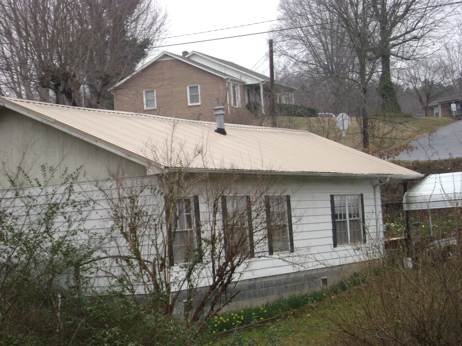 Tan metal roof on a white sided house set into a hillside — Commercial Roofing by Roofing Brothers in Dunedin