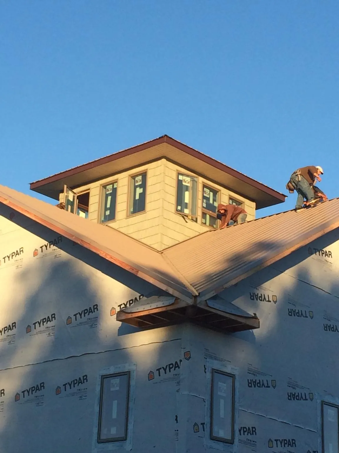 Roofers working around a rooftop cupola on a new metal roof at sunset — Roof Waterproofing in Dunedin by Roofing Brothers